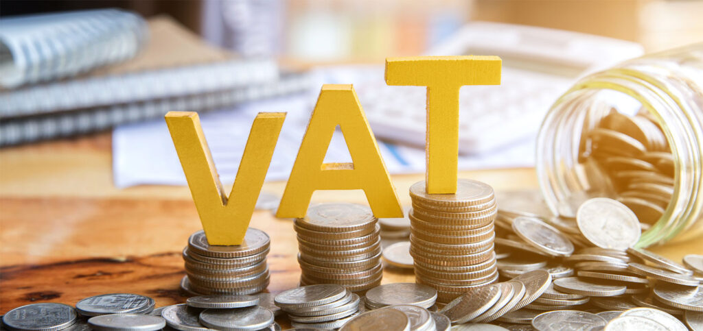 VAT sign sitting on top of coins piled up on a desk